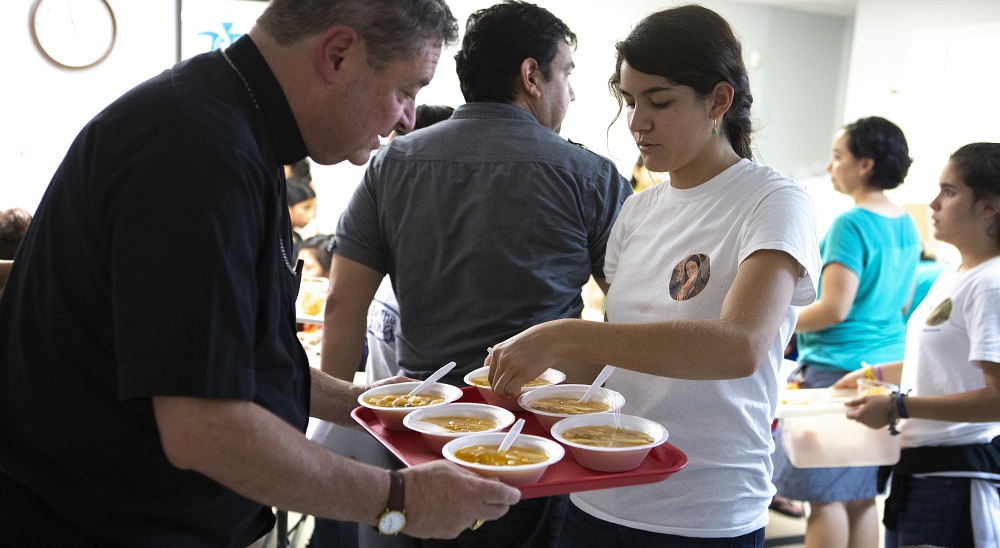 Bishop Robert Brennan, auxiliary bishop of Rockville Centre, N.Y., helps a volunteer at a Catholic Charities-run respite center in McAllen, Texas, serve soup July 1 to immigrants recently released from U.S. custody. (CNS/Chaz Muth)