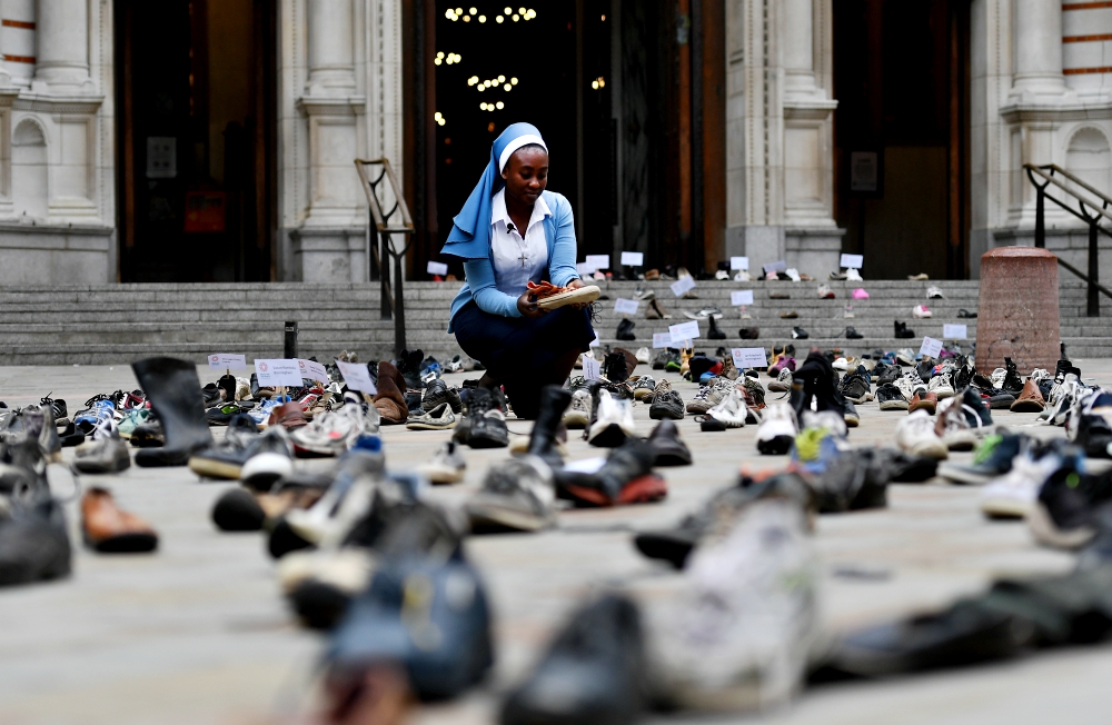 Sister Clara of CAFOD, the British bishops' international relief and development agency, is seen Aug. 15 surrounded by shoes outside the Westminster Cathedral in London. Hundreds of shoes left at the cathedral are part of a campaign launched by Pope Francis and supported by tens of thousands of people across the U.K. The campaign, led by CAFOD and the Catholic Social Action Network, calls for world leaders at next month's U.N. General Assembly to back global agreements aimed at assisting refugees and migrants. (CNS / EPA / Andy Rain)