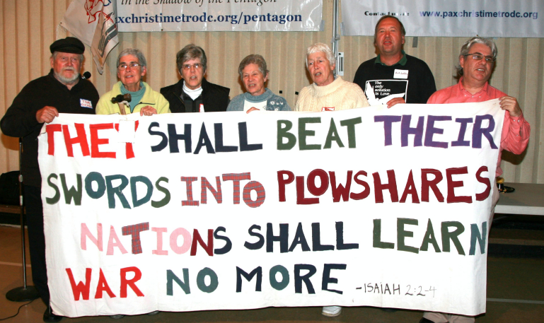 Seven plowshares activists seen together at the Pax Christi event Sunday. They are holding a sign created by the late Philip Berrigan, who participated in the first action in 1980. (Photos courtesy of Ted Majdosz)