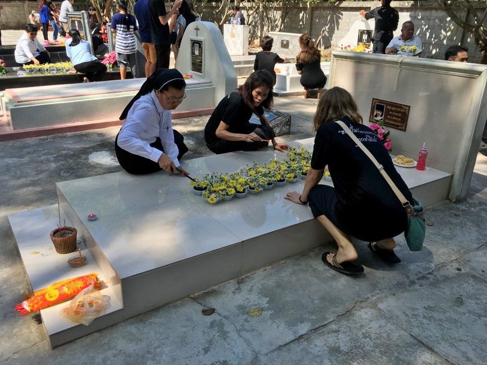 Women light candles alongside offerings of food and flowers at an annual memorial held at a Catholic cemetery near the Garden Community in Nong Khai. (Lauren Magee)