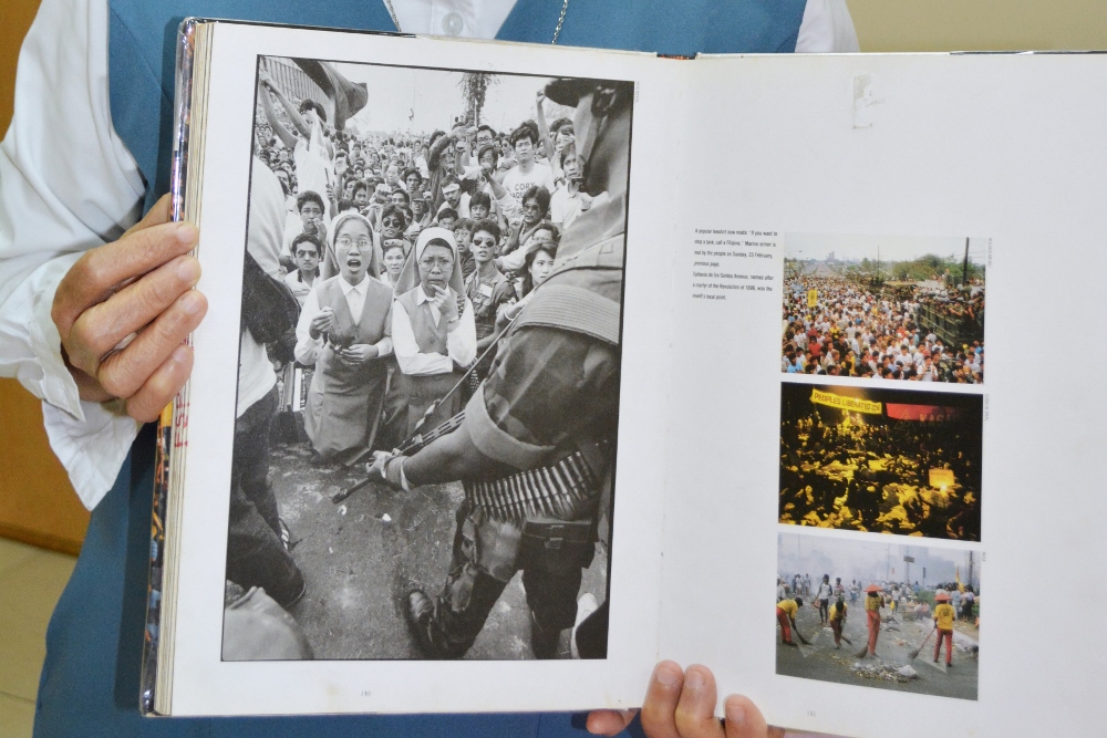 Sr. Porferia Ocariza, a member of the Daughters of St. Paul, holds a book on the People Power uprising in the Philippines 30 years ago to oust dictator Ferdinand Marcos. She is still recognized today for her stunned expression, left image, as military tanks approached. (CNS photo / Simone Orendain)