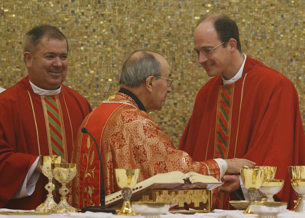 Cardinal Velasio De Paolis, the then-papal delegate in charge of governing the Legionaries of Christ, center, greets Fr. Sylvester Heereman, a member of the Legion’s general council during the sign of peace during a Jan. 8, 2014, Mass in Rome. At left is the late Fr. Alvaro Corcuera, then-director general of the congregation. (CNS/Paul Haring)