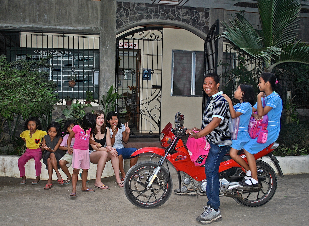 Students prepare to head home after school while younger children play outside Fatima Integrated School inside their farm compound in San Agustine, Iriga City, with a Kolping volunteer from Germany. (N.J. Viehland)