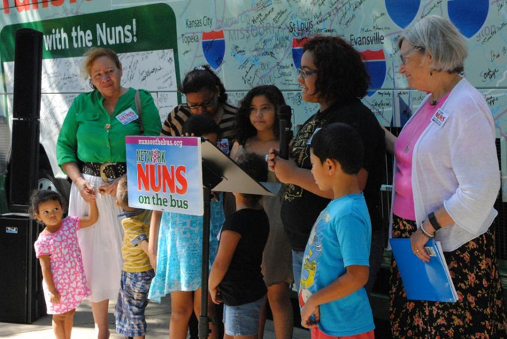 Katherine Meza, second from right, tells the crowd gathered in front of St. Anthony Church about how she and her five younger siblings are under the care of their grandmother, standing left, in green, after their parents were deported to Honduras in May. Social Service Sr. Simone Campbell, right, offers comfort during the emotional story. (GSR photo / Dawn Cherie Araujo)