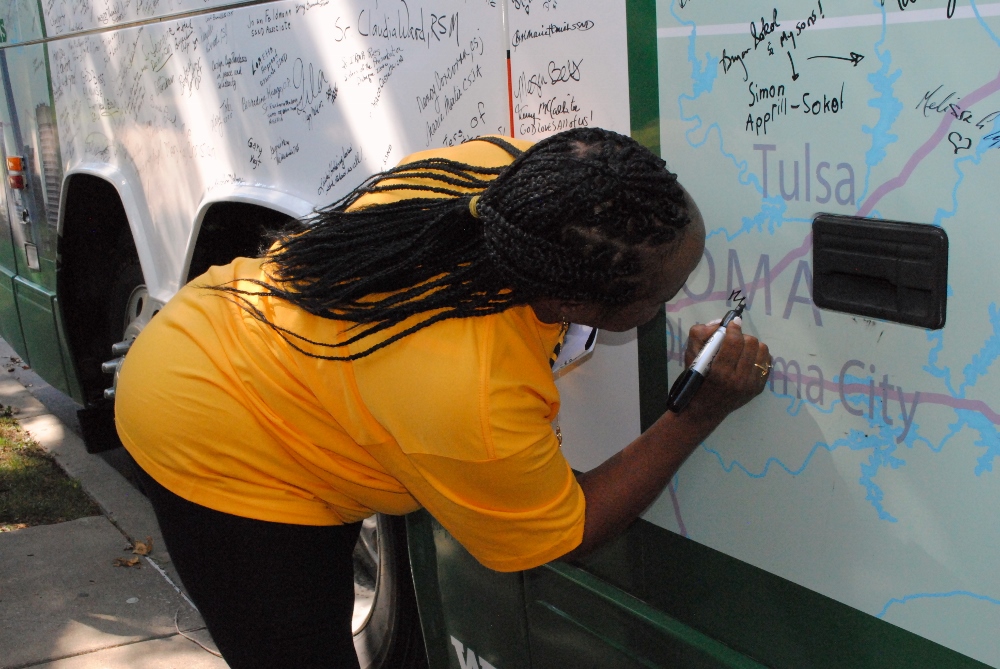 Jeanette Hutchinson, one of the people who shared her story at the Nuns on the Bus stop Sept. 11, signs the bus in support of the sisters' call to "Bridge divides and transform politics." Hutchinson is a home healthcare worker who juggles assignments from two agencies providing her 40 hours of work per week, but since her wage averages $9 an hour, she works another full-time job on weekends to make ends meet. (GSR photo / Dawn Cherie Araujo)