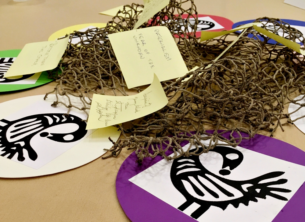 Table centerpieces at the racism conference were fishnets symbolizing the tangled web of racism all are caught in, surrounded by depictions of a mythological bird moving forward while looking back. Participants wrote ways racism has affected them on Post-It Notes on the first evening of the conference. (Pamela Schaeffer)