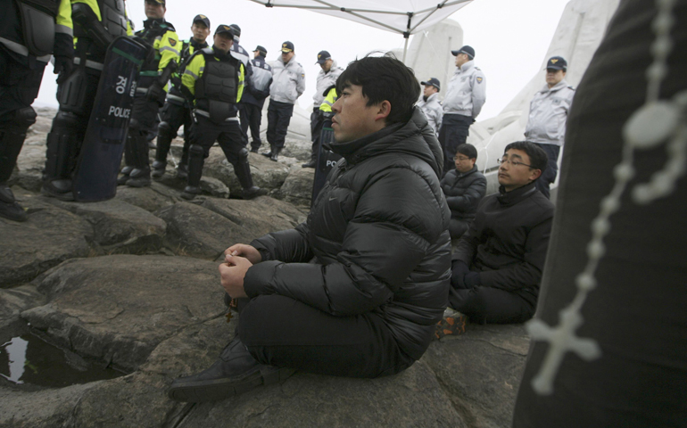 A priest prays the rosary as policement surround him and other clergy holding a sit-in protesting construction of a new naval base on Jeju Island, South Korea, in March 2012. (CNS/Reuters/Lee Myung-ik)