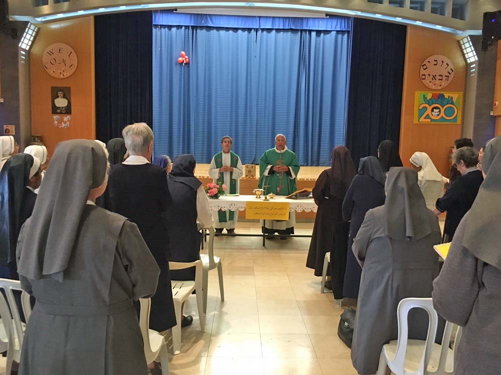 Abouna Hana Kaldani, right, and Abouna Marco celebrate Mass at the theater of the Salesian Sisters School of Nazareth, where Natalia Liviero volunteers. Note the welcome signs are in Hebrew on the top right above the picture of the 200 years of the birth of St. Don Bosco, founder of the Salesian congregation: It reads Bruchim Hava'im, and in English on the top left, above the picture of Maria Domenica Mazzarello, founder of the female Salesian congregation, Mary Help of Christians. (Natalia Liviero)