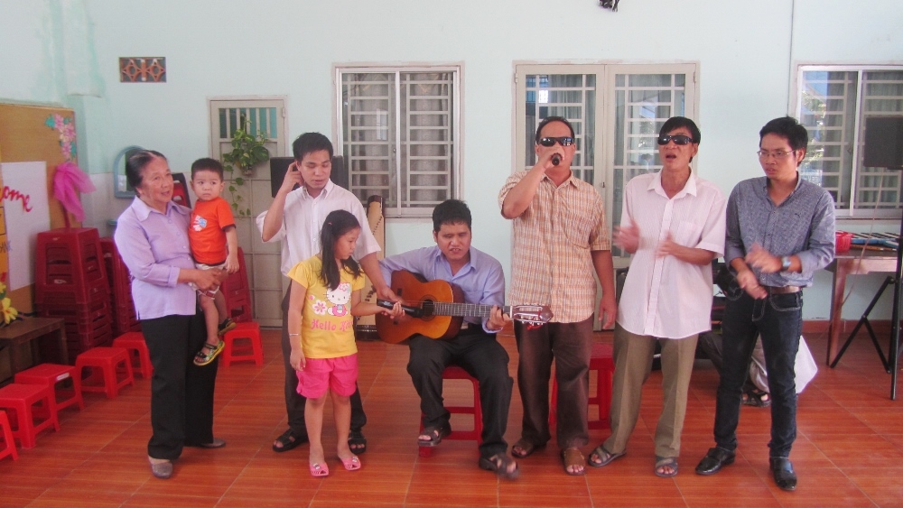 Sr. Elizabeth Tran Thi Quynh Giao, left, holds a blind man's child as people who used to stay at the Huynh De Nhu Nghia Center sing songs and play the guitar at a gathering. (GSR photo / Joachim Pham)