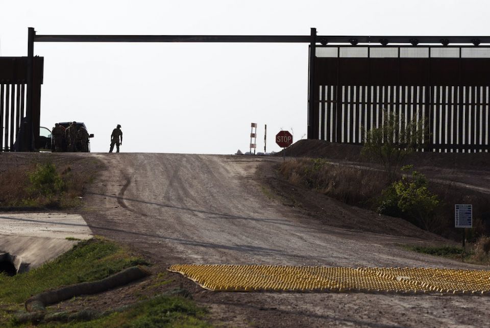 An official stands in a large opening of the border fence, a checkpoint