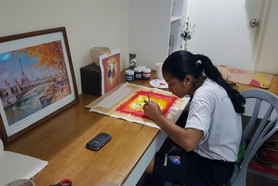 Young Filipino girl sitting at a desk painting