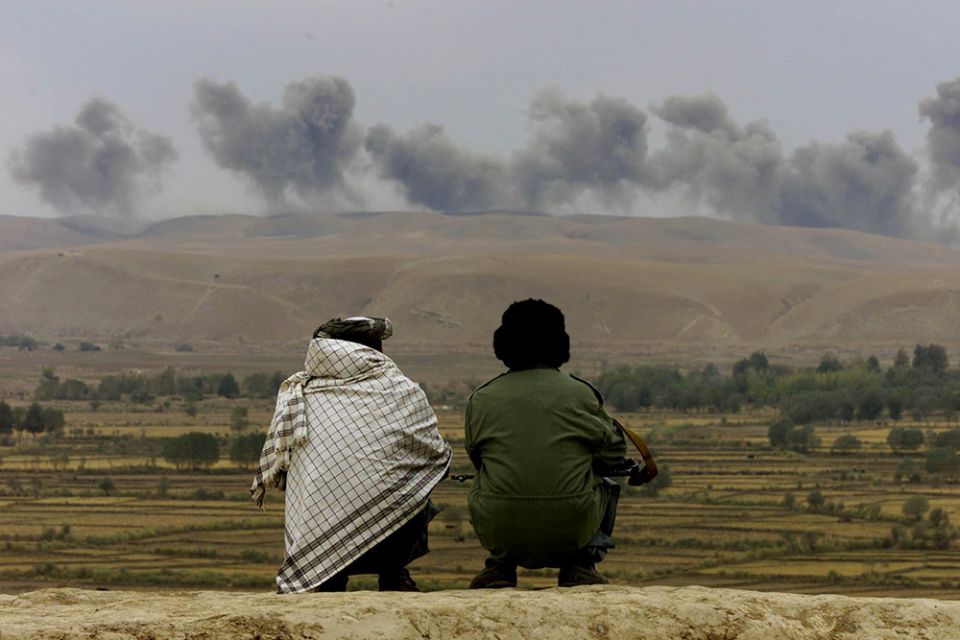 Two Northern Alliance soldiers near the village of Ai-Khanum in northern Afghanistan watch dust and smoke rise after explosions at Taliban positions Nov. 1, 2001. (CNS/Reuters/Vasily Fedosenko)