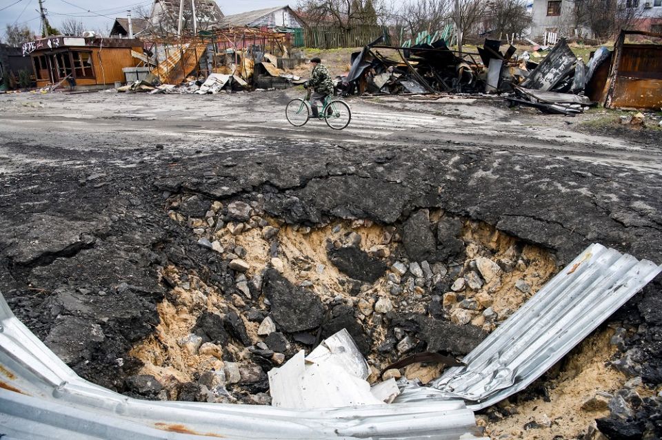A local resident rides a bicycle past a bomb crater April 6 in the village of Demydiv, outside Kyiv, Ukraine. (CNS/Reuters/Vladyslav Musiienko)
