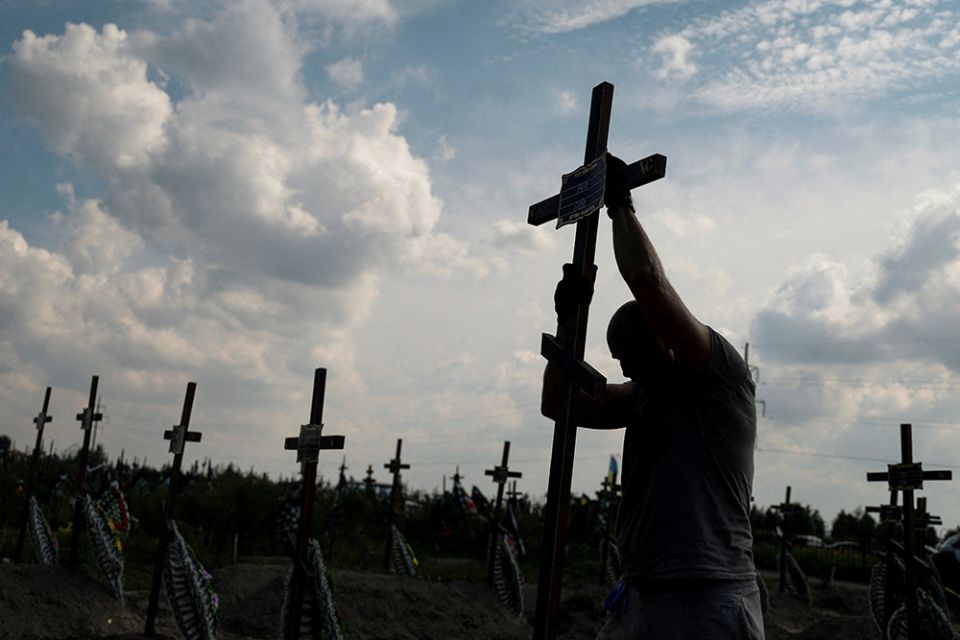 A volunteer places a cross with a number on a grave of an unidentified person during an Aug. 17 mass burial ceremony in Bucha, Ukraine, as Russia's attack on Ukraine continues. (CNS/Reuters/Valentyn Ogirenko)