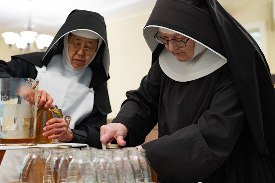 Sr. Margaret Muraki, left, and Mother Emily Ann Lindsey, both All Saints Sister of the Poor, screw caps onto jars of honey produced by bees on the sister's property in Catonsville, Maryland, on Aug. 16. (CNS/Catholic Review/Kevin J. Parks)