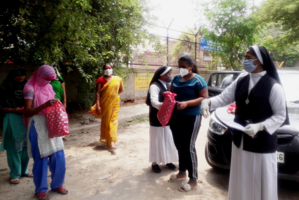 Sacred Heart Sr. Celine George Kanattu, far right, asks migrant workers to use social distancing. Catholic youth Sona Viji, dressed in blue and black, and Sr. Lucy Kizhakedath assist Kanattu to distribute clothes. (Jessy Joseph)