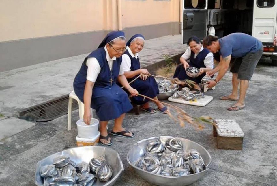 The Missionary Sisters Servants of the Holy Spirit-Northern Province provide seafood to day laborers, people whose jobs disappeared during the pandemic, in Quezon City, Philippines. (Sr. Angel C. Libron) Catholic sisters sitting in chairs in the street with baskets of fish to give away