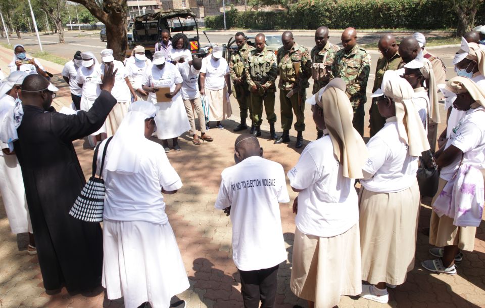 Fr. Shadrack Malo blesses the security officers and Franciscan Sisters of St. Anna in preparation for their peace campaign July 16. The caravan moved around Kisumu town and neighboring towns in Kenya to sensitize people to peaceful elections. 