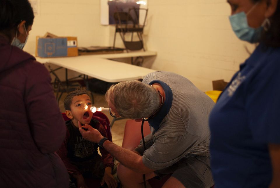 A doctor using a flashlight to look into a little boy's mouth
