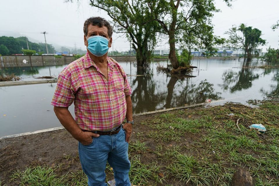 Edilio Bautista Tinoco, a cacao farmer, in the flooded Los Castanos neighborhood of Choloma, Honduras. The garment factory in the background employs 30,000 people. (Gregg Brekke)
