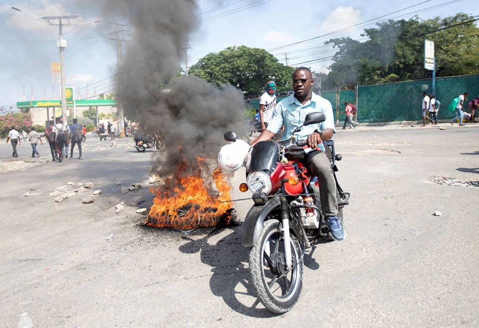 A man in Port-au-Prince, Haiti, drives his motorcycle past a burning barricade Oct. 20, 2021, as demonstrators take part in a protest against high prices and fuel shortages. (CNS/Reuters/Ralph Tedy Erol)