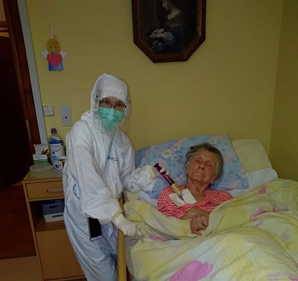 A Franciscan Sister of Love and Penance cares for a COVID-19 patient in Poland. Thousands of sisters in Poland have volunteered and worked in hospitals and health care centers during the pandemic, including 32 sister-doctors and 1,020 sister-nurses. A health care worker in personal protective equipment administers treatment to an elderly woman in bed because of COVID-19