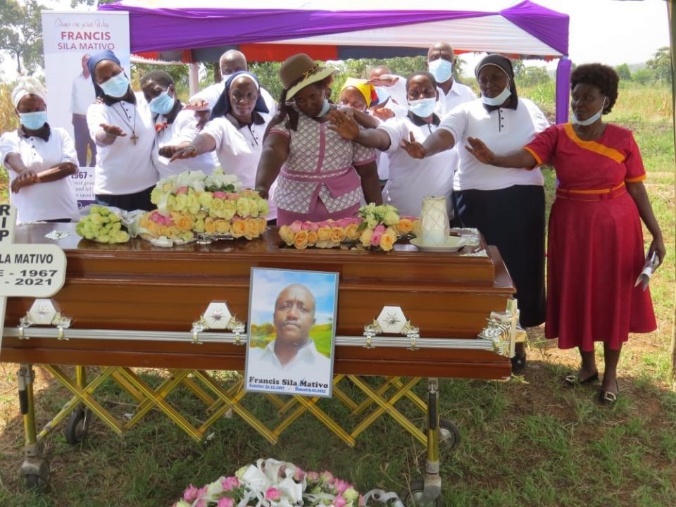 Women, including sisters in habits hold their hands over the casket to pray under a tent