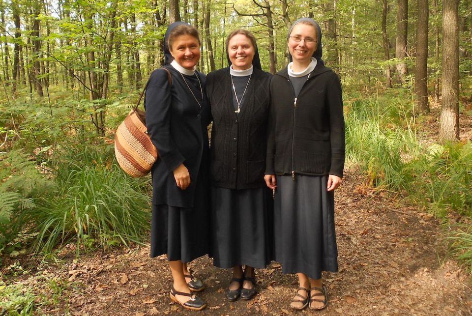 Three Catholic sisters in habits pose together in a wooded area