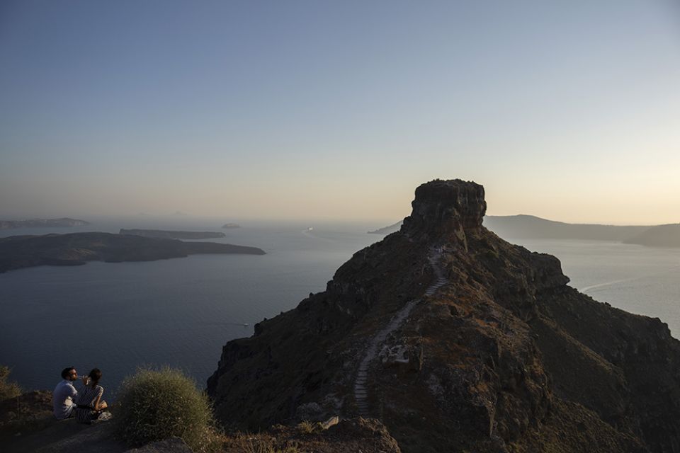 A couple drink wine in front of the rocky promontory of Skaros on the Greek island of Santorini June 15, 2022. The Catholic Monastery of St. Catherine was founded at Skaros in 1596, but after an earthquake it was moved to the nearby village of Thira. (AP)