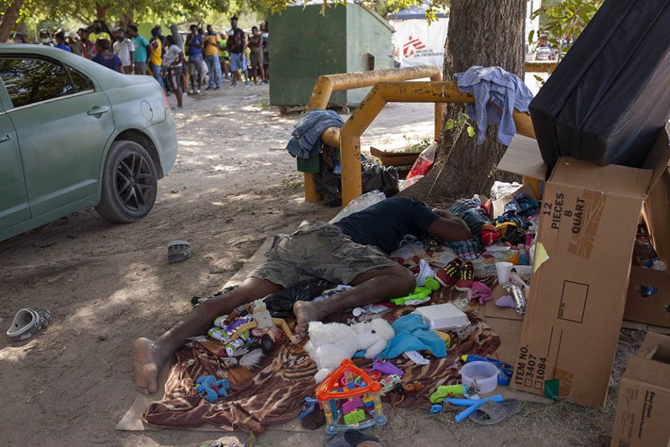 An immigrant uses a slab of cardboard as a bed to catch a nap while others line up for services Sept. 22 at an immigration camp in Ciudad Acuña, Mexico. (Nuri Vallbona)