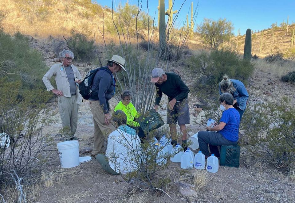 School Sister of Notre Dame Judy Bourg (seated at right) and other volunteers write upbeat messages to migrants on water jugs at a drop-off site in the Sonora Desert in October 2021. (Peter Tran)