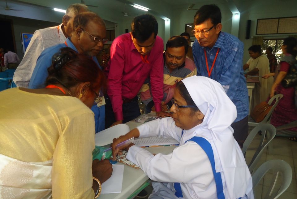 A habited sister in white and blue points to papers on a desk while others gather around to listen