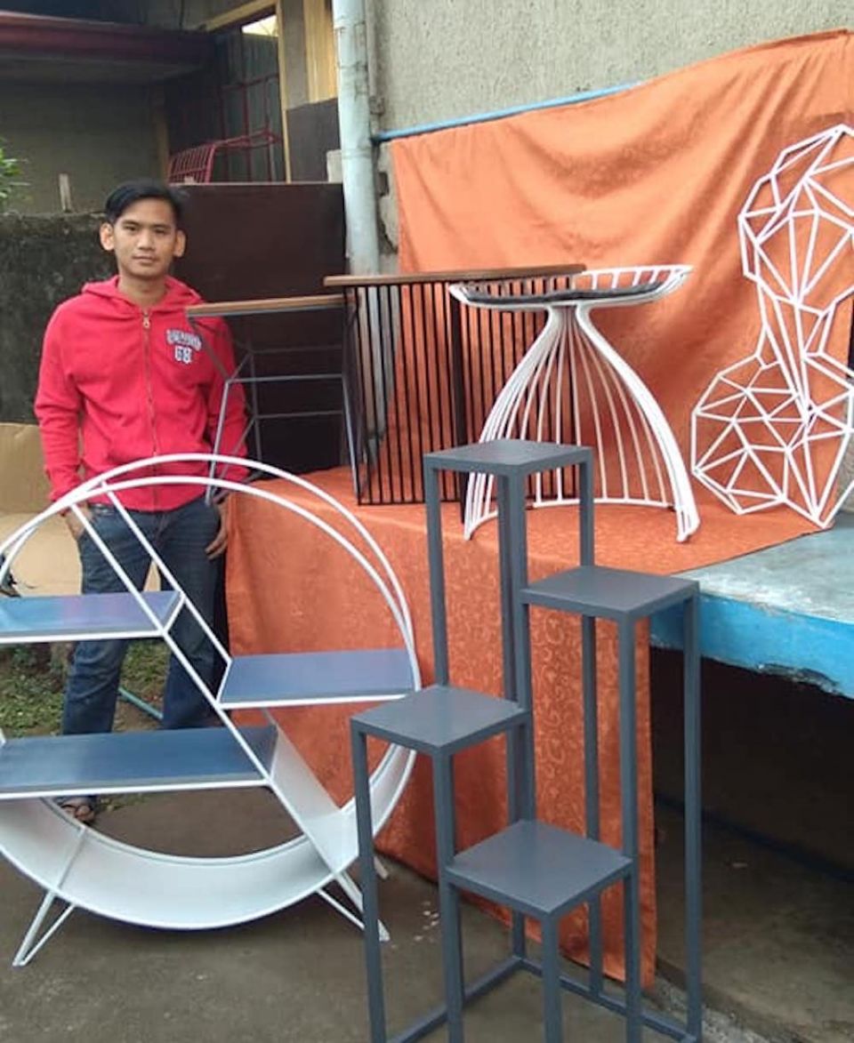 Raymart Montinola started his own furniture-making business with a loan from the Missionaries of Mary after he completed the Second Chance program. (Courtesy of the Missionaries of Mary) Young Filipino man stands by shelves and other furniture he made, Raymart Montinola