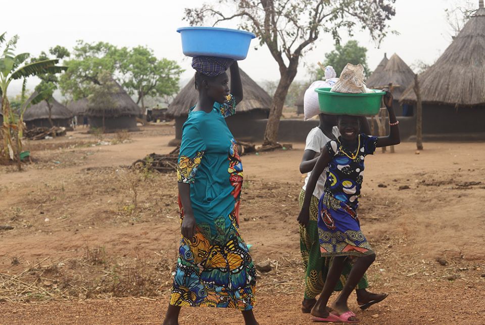 Young refugee women carry corn flour on their heads at the Palabek refugee camp in northern Uganda. Many refugees produced enough corns and beans to feed their family amid the COVID-19 pandemic after receiving seeds and farming support to help mitigate