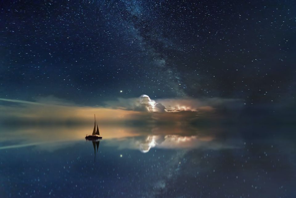 A silhouetted sailboat in the night under the stars (Unsplash/Johannes Plenio)