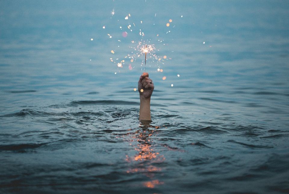Image of a person holding a lit sparkler above the water (Unsplash/Kristopher Roller) Image of a person holding a lit sparkler above the water (Unsplash/Kristopher Roller)