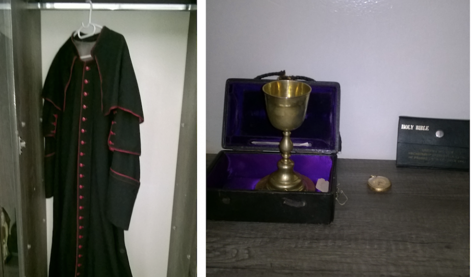 Roman Catholic cassock, black with red buttons, hanging in a closet; a golden chalice sitting in a purple velvet lined case next to a Bible