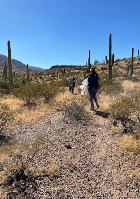 After dropping off water on a migrant trail in the Sonoran Desert, volunteers walk back to their vehicles with empty water bottles in October 2021. (Peter Tran)