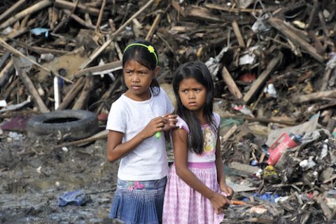 In this 2013 photo, two girls from Tacloban City, Philippines, stand in front of damaged property and debris left by Super Typhoon Yolanda/Haiyan. (United Nations)