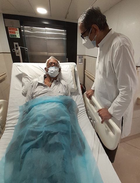 Jesuit Fr. Stan Swamy lies in his hospital bed in Holy Family Hospital, Mumbai, western India. His visitor is Fr. Frazer Mascarenhas, the only Jesuit that Swamy was allowed to see during nine months of incarceration. (Courtesy of Frazer Mascarenhas)