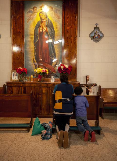 Backs of a kneeling woman and young boy before an altar with the Virgin of Guadalupe