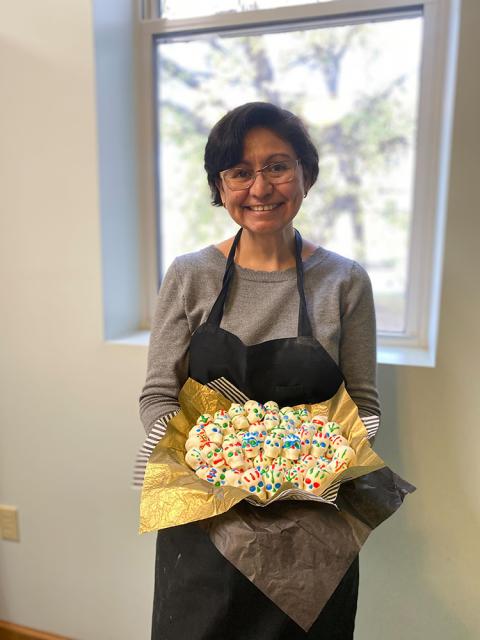 A woman with short black hair and glasses smiles and holds a tray of sugar skulls