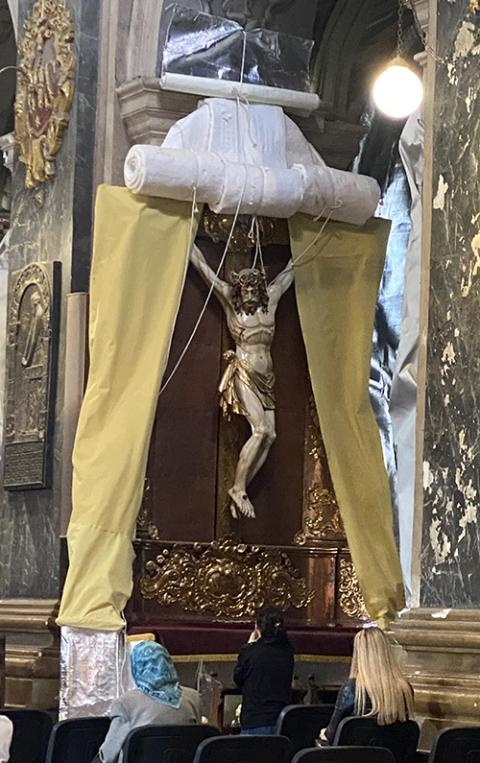 Ukrainians pray before a crucifix at the Garrison Church of Sts. Peter and Paul in Lviv, Ukraine, Aug. 3, 2022. A roll of thick padding hangs above the crucifix to protect it in case the church is attacked. (Rhina Guidos) 