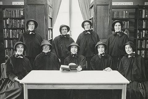 A black-and-white photo of a group of nuns in the mid-20th century pose for a photograph in a library