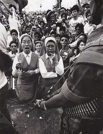 An iconic photo of two Daughters of St. Paul kneeling in the middle of civilians preventing the movement of military tanks on EDSA. The photo was taken by Pete Reyes, first published in Manila Times, and reproduced in other newspapers reporting the bloodless revolution. (Manila Times/Pete Reyes)