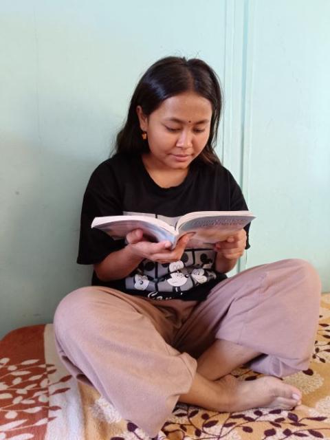Sabita sits with legs crossed and holds a book.
