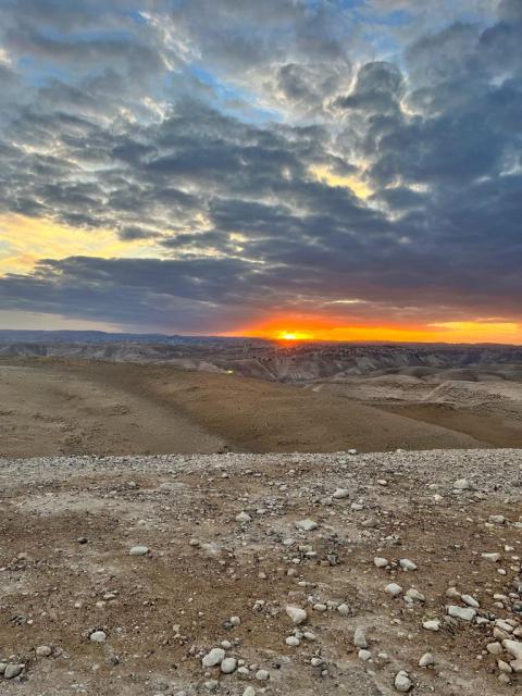 The sun sets, with orange light, amid a cloudy blue and white sky and the desiert.