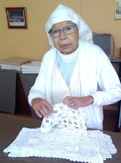 The sister stands at a table, handling textiles. 