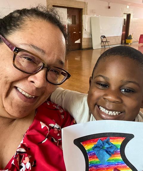 United Stand staff member Miriam Munoz poses with a child and the art he created at a United Stand program. (Courtesy of United Stand)