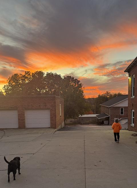 Author Helen Mueting walks outside with a black lab at the Benedictine monastery in Atchison, Kansas, as a fall sunset colors the background. (Courtesy of Helen Mueting)
